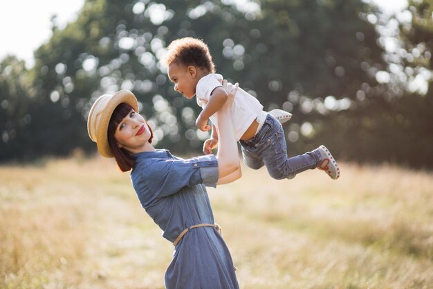 Caucasian mother playing with her african son on nature