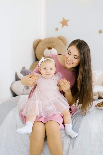 A Caucasian mother puts her one year old daughter on her lap and looks at her in the children's room in the house and smiles