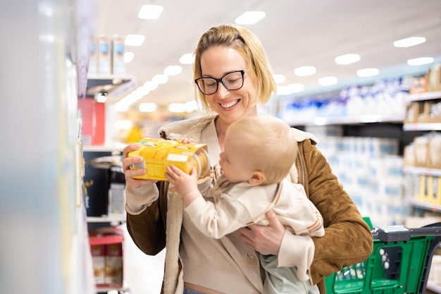 Photo caucasian mother shopping with her infant baby boy child choosing products in department of