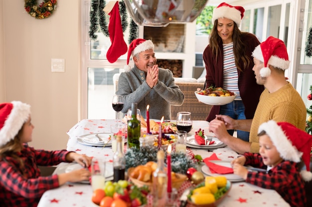 サンタ帽子をかぶった白人の多世代家族がクリスマスの食事を食べる。家族のクリスマスの時間とお祭りを家で一緒に過ごします。