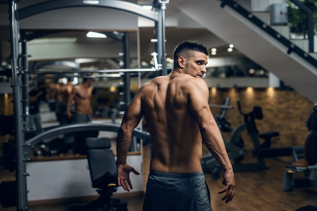 Uomo senza camicia muscolare caucasico che posa in palestra. schiena girata.