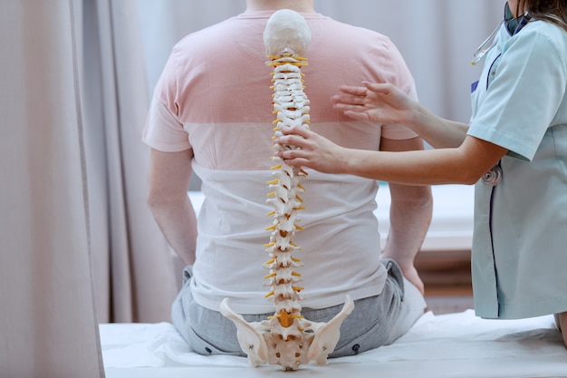 Photo caucasian nurse holding spine model against the patients backs. clinic interior.