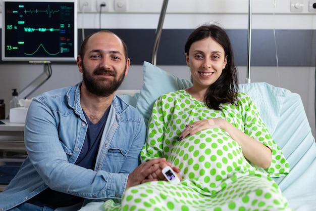 Кавказские родители обсуждают отцовство перед кесаревым сечением в больничной палате. Беременная женщина лежит в постели, утешается мужем, готовится к родам в родильном доме