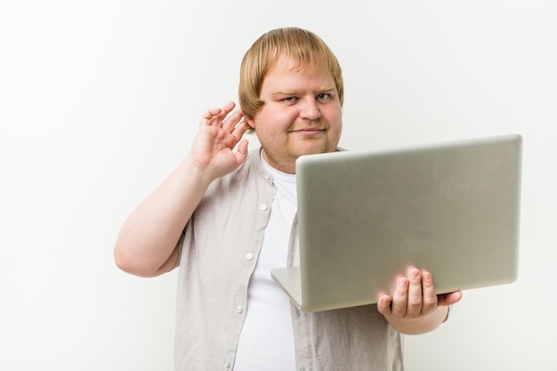 Caucasian plus size man holding a laptop trying to listening a gossip.