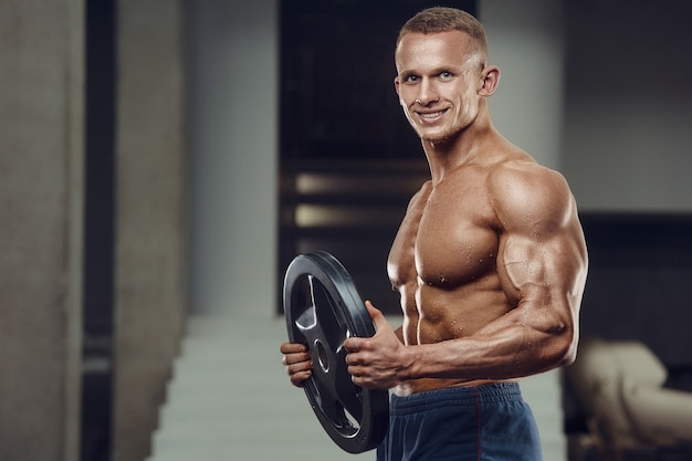 Caucasian power athletic man training pumping up biceps muscles. Strong bodybuilder with six pack, perfect abs, triceps, chest, shoulders in gym. Fitness and bodybuilding concept