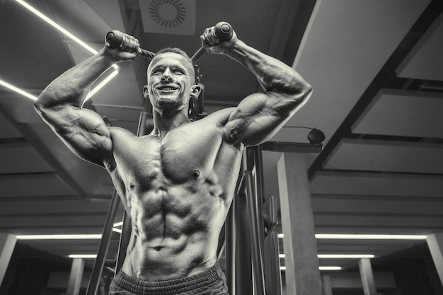 Caucasian power athletic man training pumping up triceps muscles. Strong bodybuilder with six pack, perfect abs, triceps, chest, shoulders in gym.