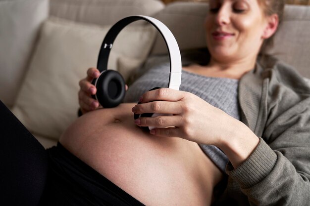 Foto donna incinta caucasica sdraiata sul divano e con le cuffie sull'addome