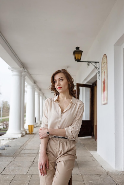 Caucasian pretty girl with red lips curly hair in stylish beige blouse outdoors