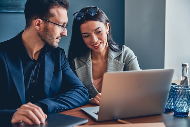 Caucasian pretty woman and handsome colleague talking together and using notebook at the workplace