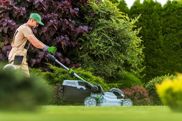 Photo caucasian professional garden worker with cordless electric grass mower working in residential backyard garden gardening and landscaping industries