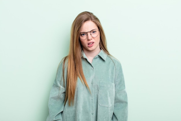 Caucasian red hair woman feeling puzzled and confused, with a dumb, stunned expression looking at something unexpected