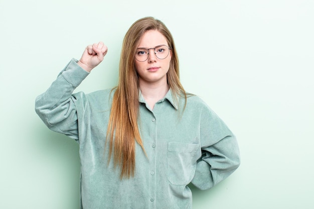 白人の赤い髪の女性は、深刻で、強く、反抗的で、拳を上げ、抗議し、革命のために戦っています