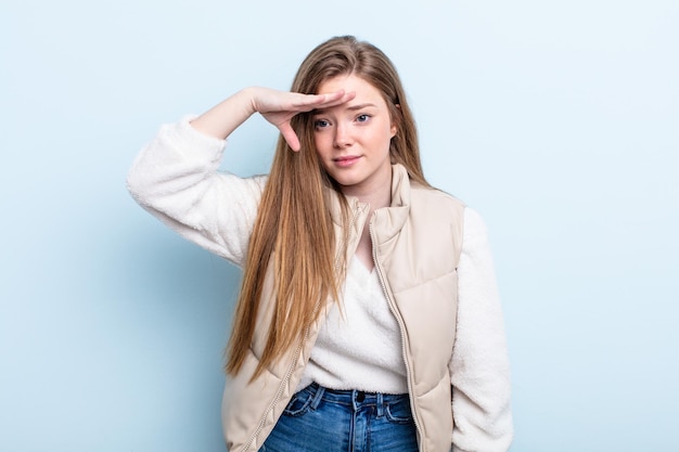 Caucasian red hair woman looking bewildered and astonished with hand over forehead looking far away watching or searching