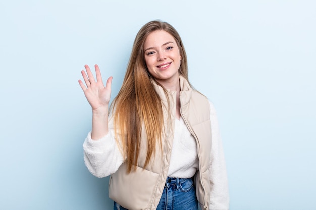 Caucasian red hair woman smiling happily and cheerfully, waving hand, welcoming and greeting you, or saying goodbye