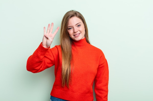 caucasian red hair woman smiling and looking friendly, showing number four or fourth with hand forward, counting down