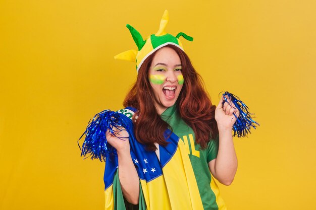 Caucasian redhaired woman soccer fan from brazil dancing wearing cheerleader pom poms