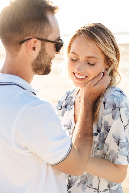 caucasian romantic couple man and woman smiling and hugging while walking on sunny beach