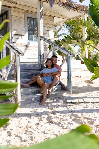 Foto giovane coppia romantica caucasica che guarda lontano mentre è seduto sui gradini di legno fuori dal cottage. inalterato, amore, insieme, vacanza, località turistica, stile di vita, spiaggia, divertimento e concetto estivo.