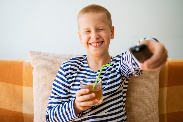 Photo caucasian school-age boy sits on a sofa in casual clothes with a remote control