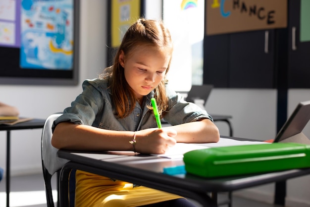 Caucasian schoolgirl sitting at desk and taking notes in school classroom