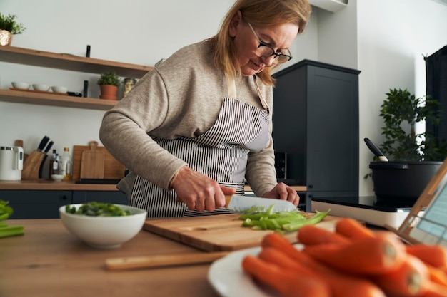 Кавказская старшая женщина разрезает овощи во время приготовления пищи на кухне