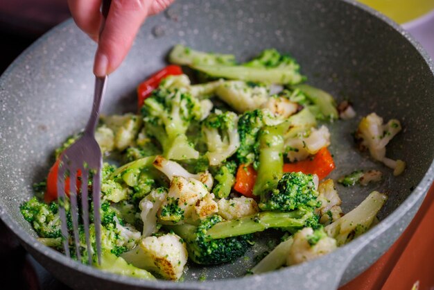 Caucasian senior woman hand with fork stirring frying vegetables in frying pan