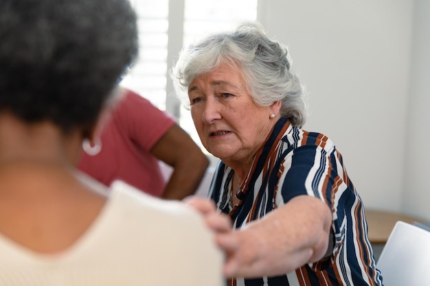 caucasian senior woman touching african american female friend and supporting her