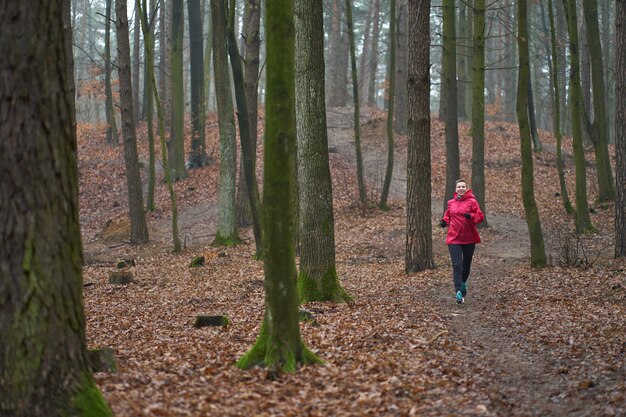 Caucasian short-haired, weared in pink raincoat woman runs in foggy forest