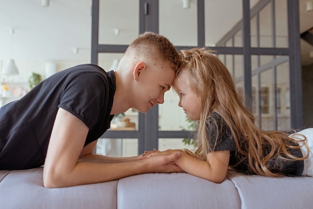 caucasian siblings  teenager boy brother and little girl sister laying holding hands on a couch