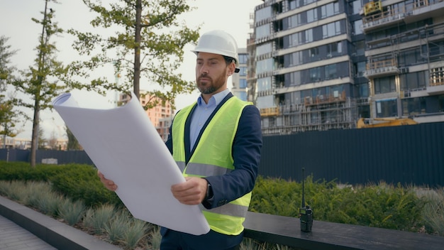 Caucasian smiling adult man in city with blueprint paper document plan work outdoors male architect