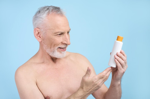 Caucasian smiling senior man holding white bottle with SPF sunscreen lotion on blue background