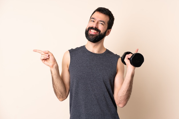 Caucasian sport man with beard making weightlifting over wall pointing finger to the side