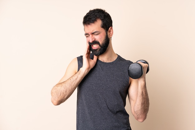 Caucasian sport man with beard making weightlifting over wall with toothache