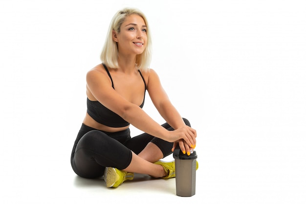 Caucasian sport woman with blonde hair listen to music with big earphones and with sport bottle for water