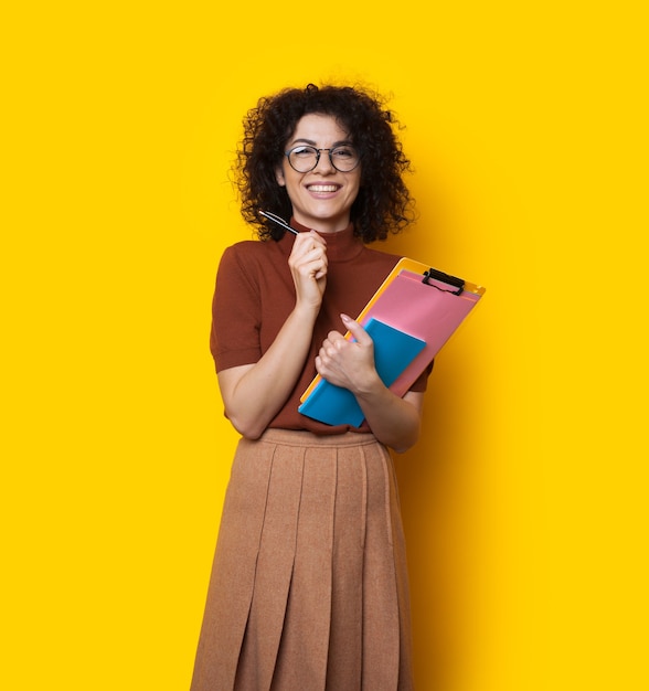 Caucasian student with curly hair is holding some books and smiling cheerfully