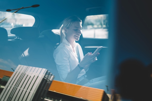 Caucasian successful female manager holding cellphone gadget sitting at backseat for passengers