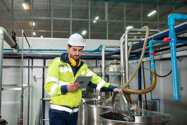 Caucasian technician engineer man in uniform with tablet checking and control boiler tanks and liquid pipeline in chemical factory production line