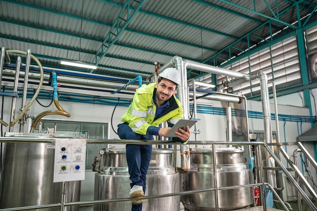 Caucasian technician engineer man in uniform with tablet checking and control boiler tanks and liquid pipeline in chemical factory production line