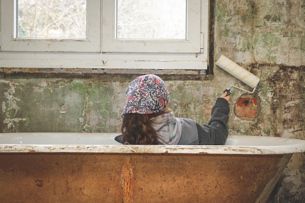 Photo a caucasian teenage girl in a bandana sits in the bathroom and holds a roller for for painting wall