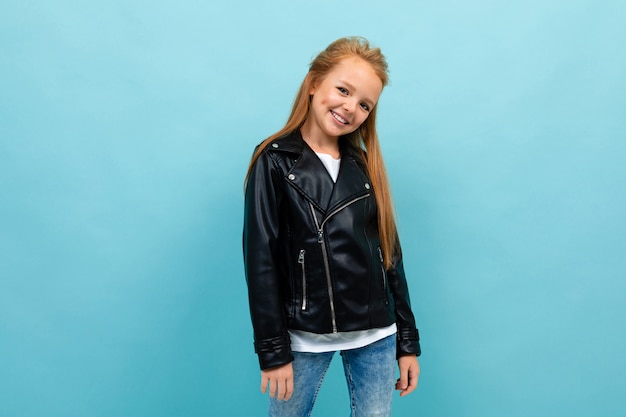 Caucasian teenager girl in black jacket and jeans smiles isolated on blue