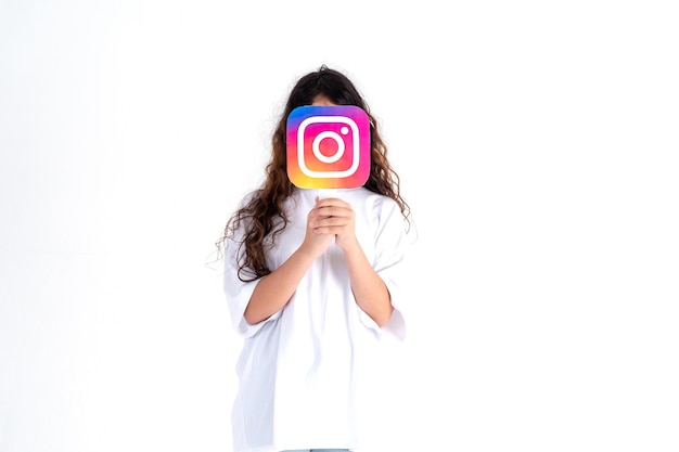 Caucasian teenager holding a Instagram logo picture in his hands on a white background