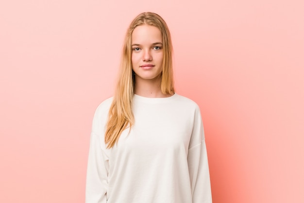 Caucasian teenager standing against a pink wall