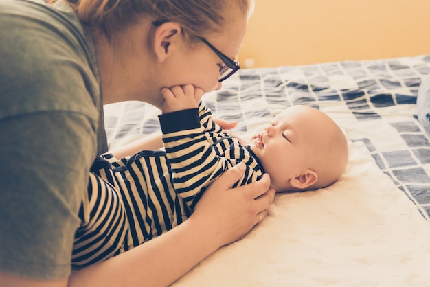 コーカサス人の優しい母親と赤ちゃんがベッドに横たわって、赤ちゃんに優しく触れます。母性、信頼と保護の概念。ライフスタイルと明るい色調