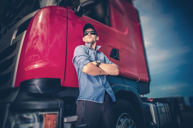 Photo caucasian trucker in his 30s and his red euro semi truck tractor transportation and shipping industry