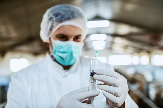 Caucasian veterinarian in protective uniform standing and holding a syringe