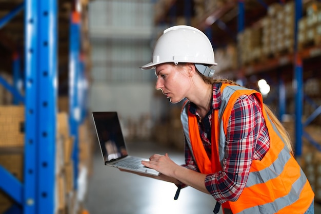 Caucasian warehouse worker checking the package using a laptop in the large distribution center