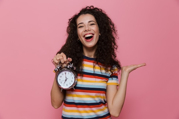 Photo caucasian woman 20s with curly hair holding alarm clock isolated on pink