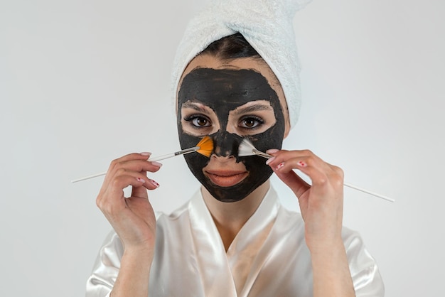 Foto donna caucasica che applica una maschera di argilla con un pennello sul viso per la cura della pelle
