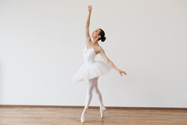 Caucasian woman ballerina in white tutu dancing on pointe with arms overhead