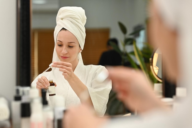 Caucasian woman in bathrobe applying drop of essential oil on back of hand doing her everyday routine at home